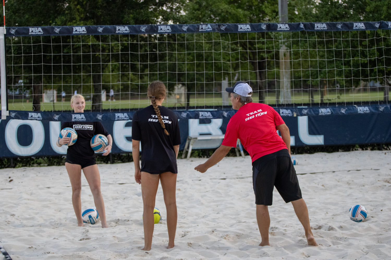 Three people playing beach volleyball on a sandy court with a net and 'FIVB' branding in the background.